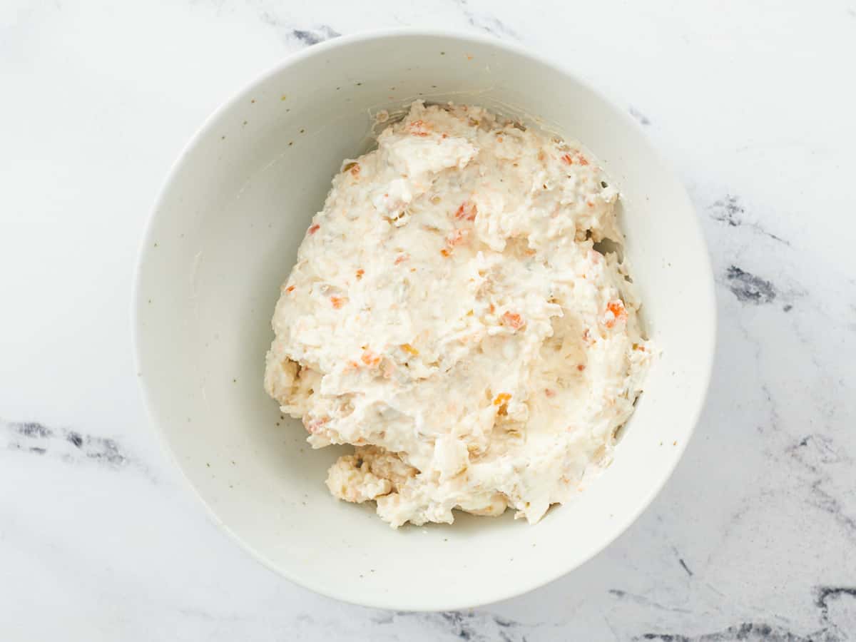 A small white bowl filled with a savory cream cheese spread inspired by pimento cheese dip on a white marble background. 