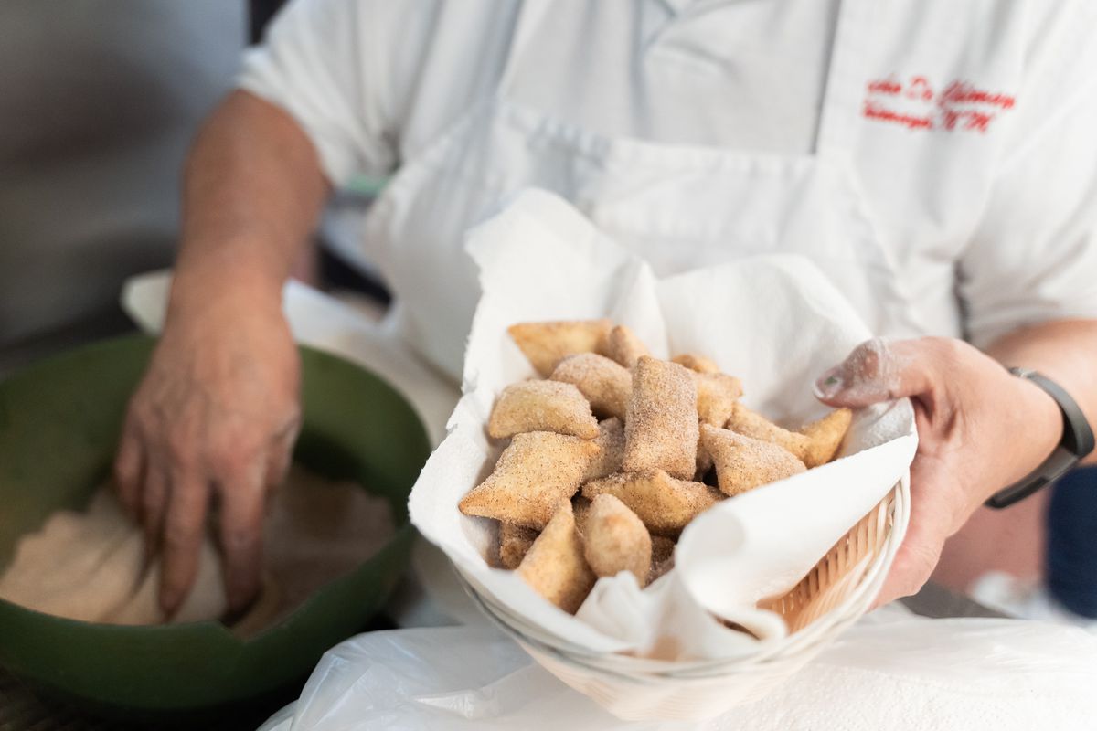 A chef holds out a basket of sopaipillas. 