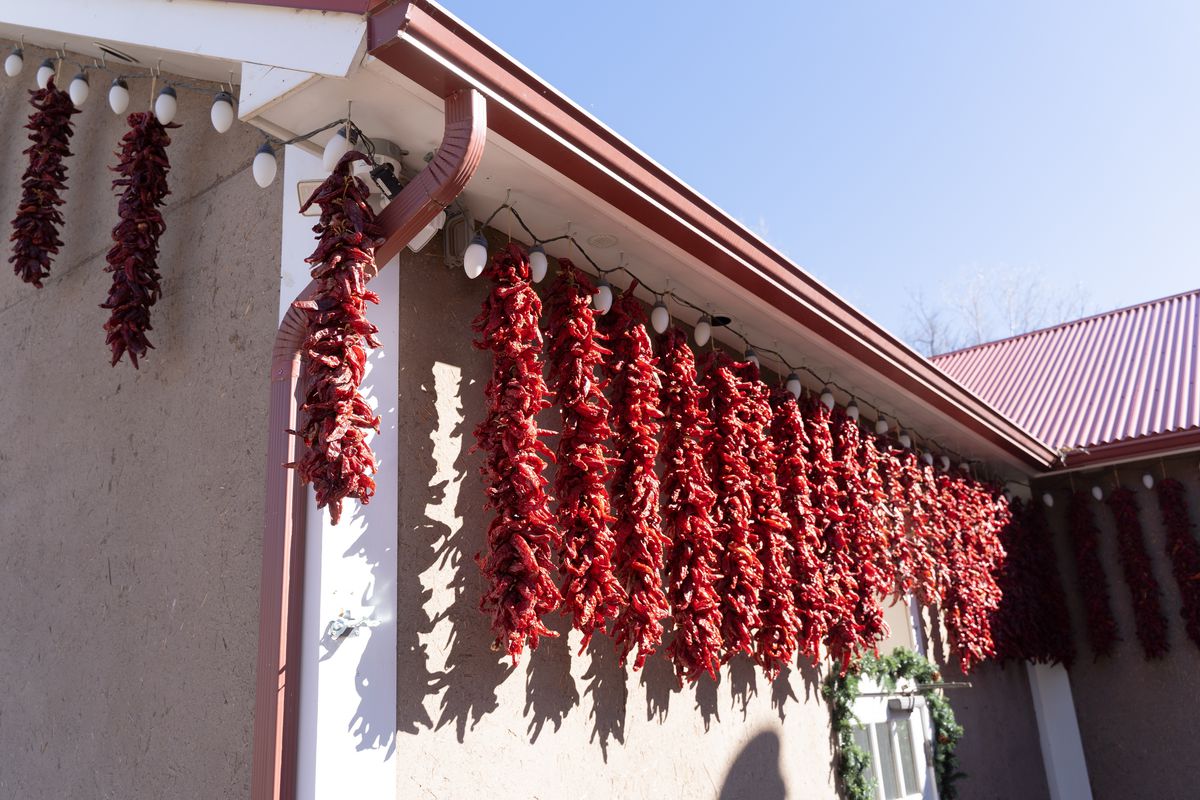 A sunny building exterior where chiles hang on strings. 